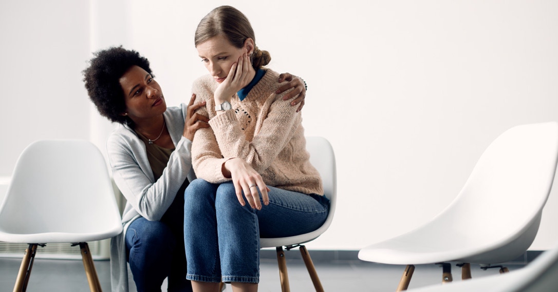 caring african american woman consoling sad woman before group therapy meeting